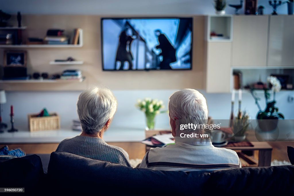 Rear view of unrecognizable senior couple looking television