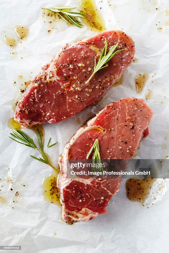 Two Raw Steaks with Marinade and Rosemary on Butcher's Paper