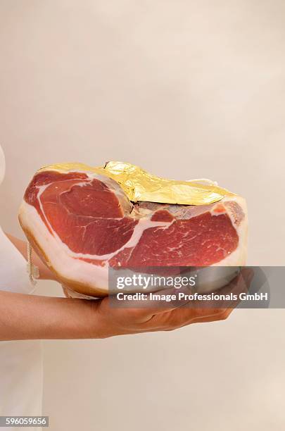 a woman holding a parma ham wrapped in gold foil - prosciutto wrapped stock pictures, royalty-free photos & images