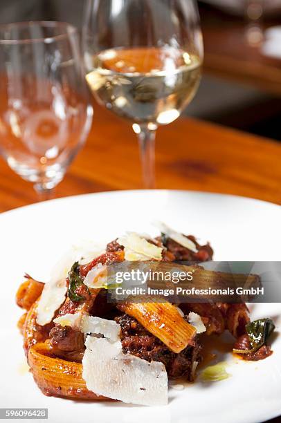 rigatoni with short ribs and shaved parmesan cheese; on a white plate; glass of white wine in background - shaved parmesan stock pictures, royalty-free photos & images