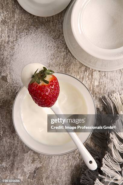 yoghurt on a spoon with a strawberry; a pot of sugar to one side - yoghurt lid stock pictures, royalty-free photos & images