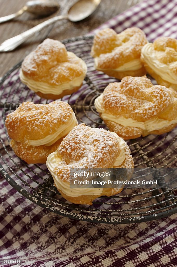 Profiteroles dusted with icing sugar, on a cooling rack