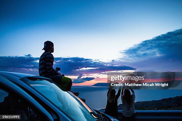 a cliffside road stop to watch the sunset - 3 guy friends road trip photos et images de collection