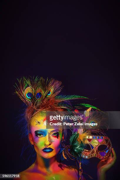 woman with colorful body painting holding a venetian mask decorated with peacock feathers - venezianische karnevalsmaske stock-fotos und bilder