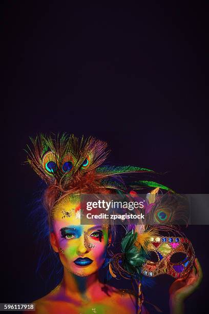 woman with colorful body painting holding a venetian mask decorated with peacock feathers - venetian mask stock pictures, royalty-free photos & images