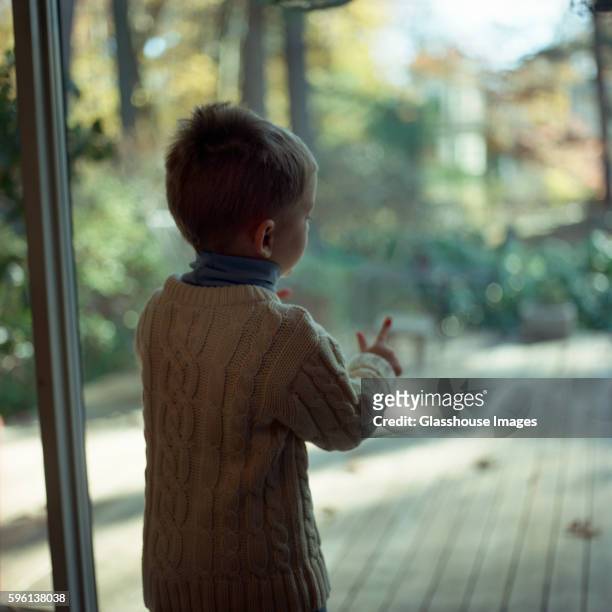 young boy in sweater at window - sliding door stock-fotos und bilder