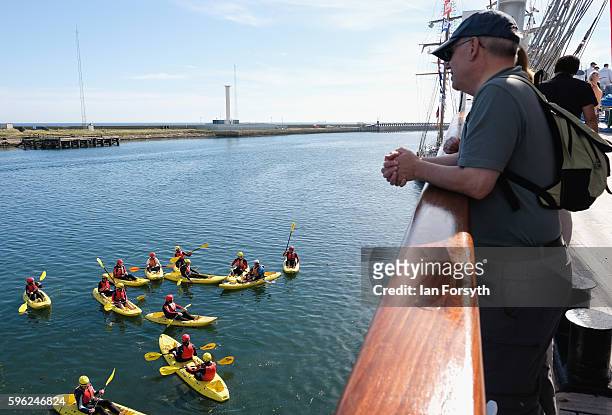 Man looks overboard from one of the ships as kayakers paddle alongside during the North Sea Tall Ships Regatta on August 27, 2016 in Blyth, England....