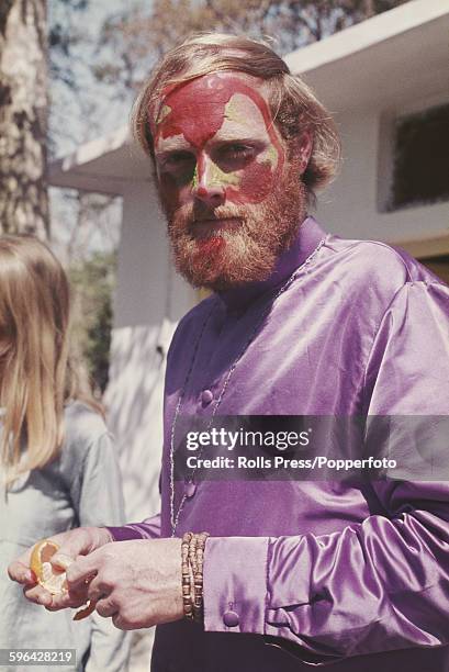 American musician, singer and founder member of the Beach Boys, Mike Love pictured with red and green face paint and wearing a purple shirt at the...