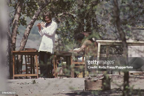 John Lennon from The Beatles pictured playing a flute as he walks barefoot through the Chaurasi Kutia ashram compound of Maharishi Mahesh Yogi near...