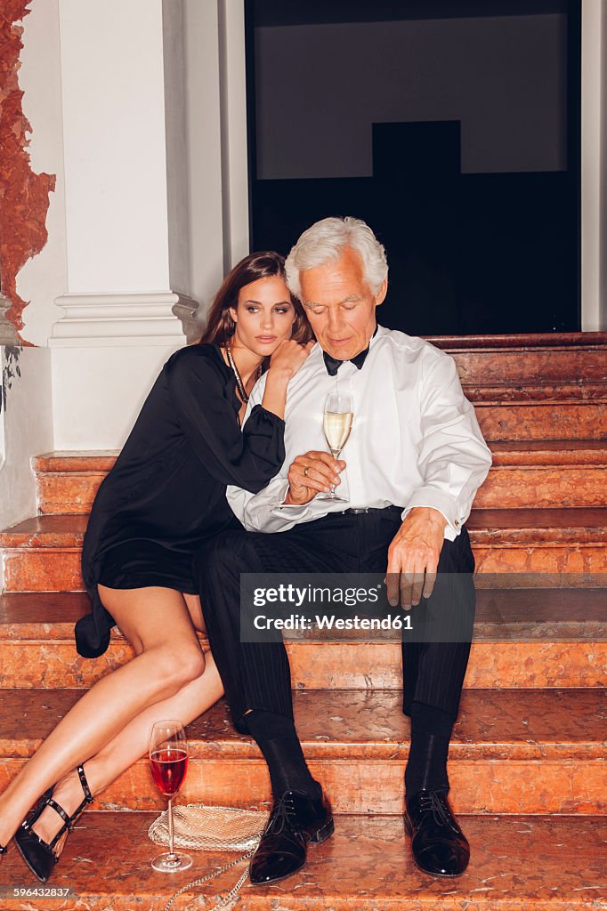 Senior man and young woman with glasses of champagne on stairs