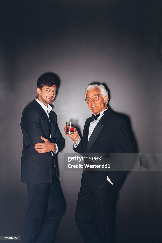 Smiling young man and elegant senior man holding drink