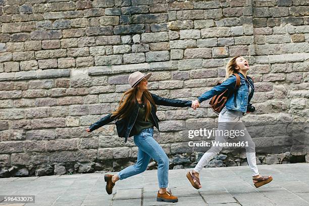 spain, barcelona, two young women running hand in hand in the city - man running city stock-fotos und bilder