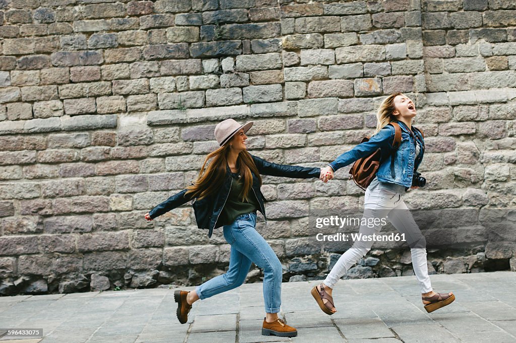 Spain, Barcelona, two young women running hand in hand in the city