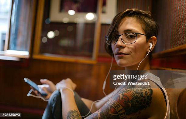 portrait of tattooed young woman listening music with earphones - tattoo shoulder stock-fotos und bilder
