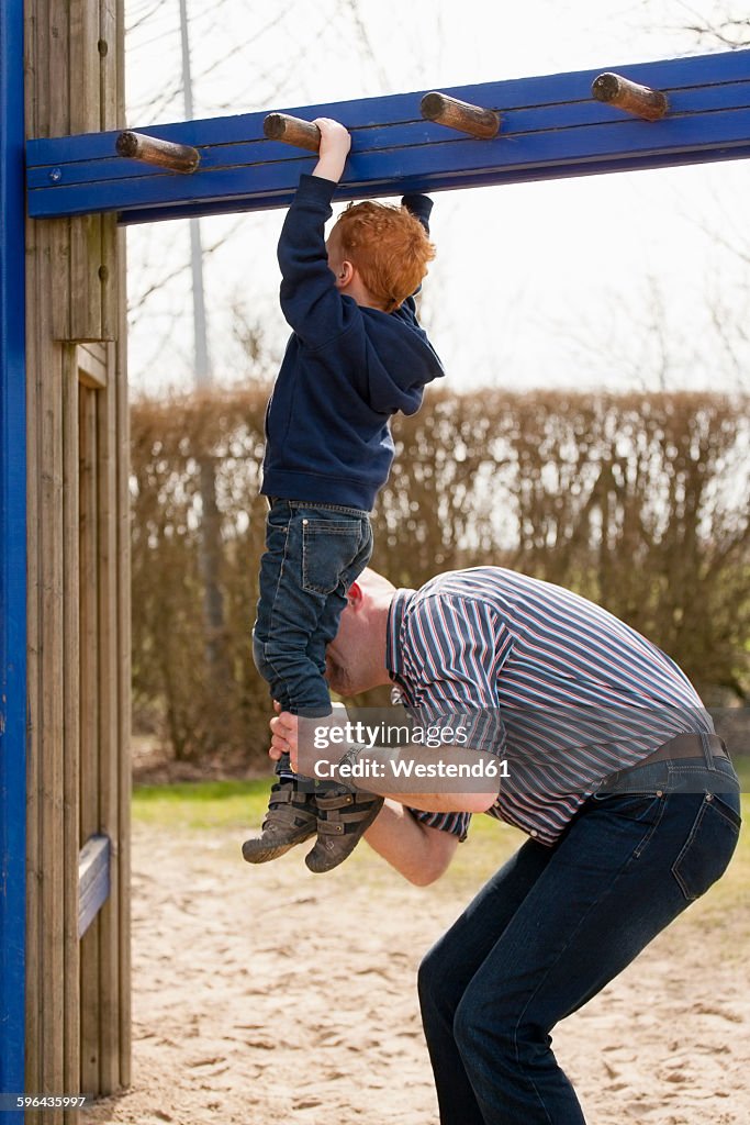 Father helping son on playground climbing on jungle gym