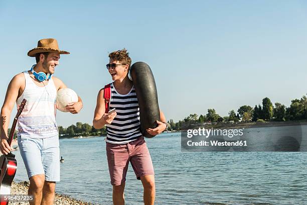 two friends with inner tube and guitar walking at the riverside - riverbank stock-fotos und bilder