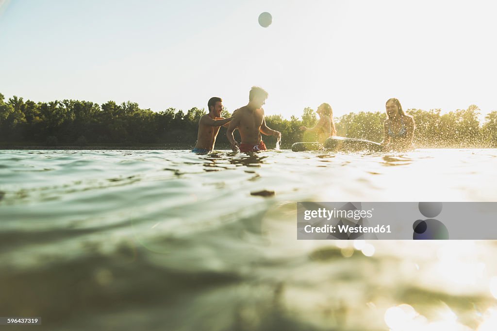 Happy friends with inner tubes and ball in water