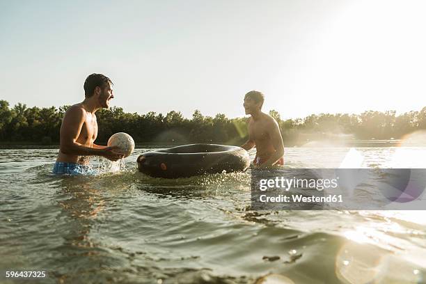 two friends with inner tube and ball in water - river bathing stock pictures, royalty-free photos & images