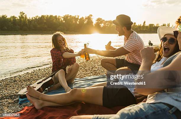 friends relaxing at the riverside at sunset - couché de soleil photos et images de collection