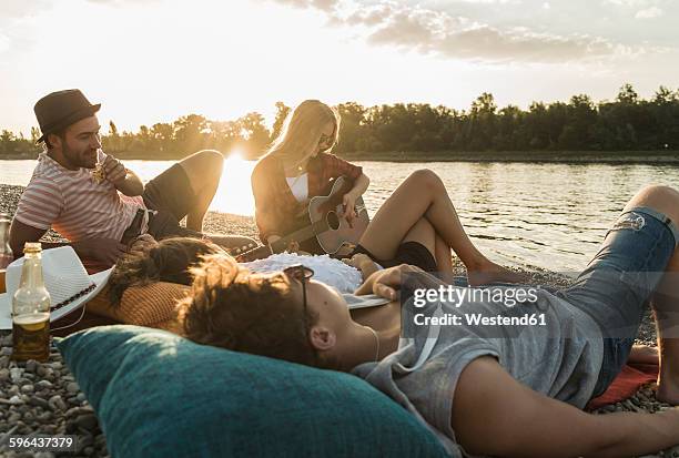 friends relaxing at the riverside at sunset - bottle rocket stock-fotos und bilder