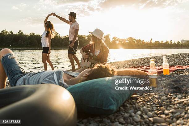 friends relaxing at the riverside at sunset - summer lights stockfoto's en -beelden
