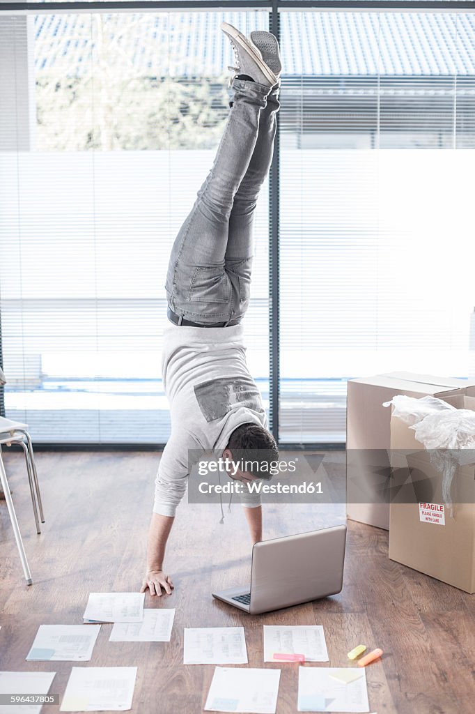 Man doing a handstand at laptop next to cardboard boxes