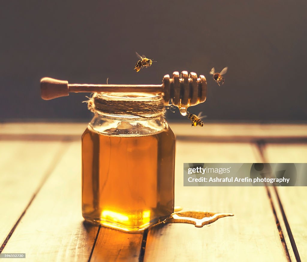 Jar of honey with honey dripper and bees