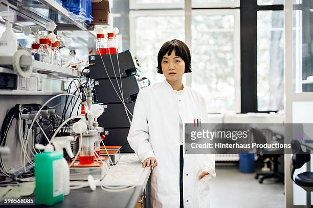 portrait of asian scientist standing in laboratory - mid adult stock-fotos und bilder