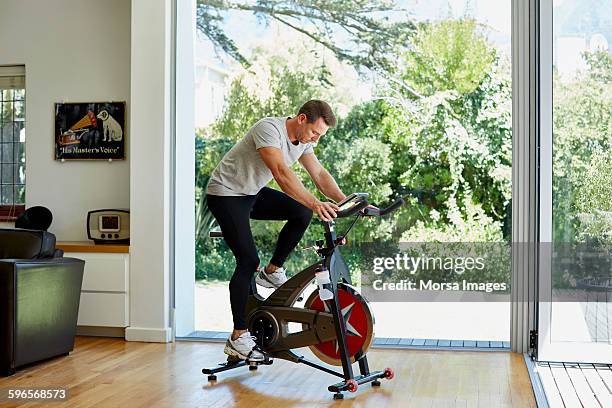 hombre haciendo ejercicio en bicicleta estática en casa - exercise bike fotografías e imágenes de stock