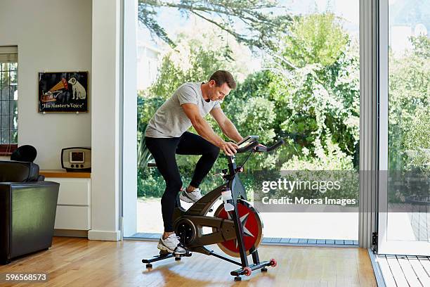 man working out on exercise bike at home - exercise room stock pictures, royalty-free photos & images