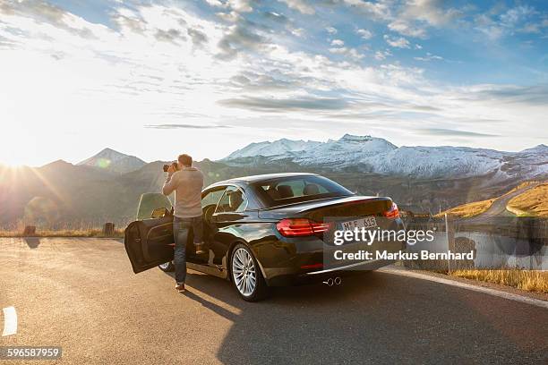 man stepping out of his car to take a picture. - sedan stock pictures, royalty-free photos & images