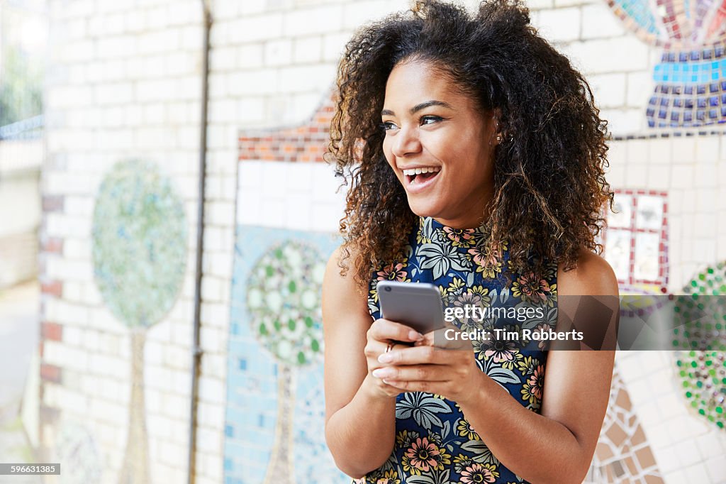 Woman with smart phone next to tiled mosaic wall