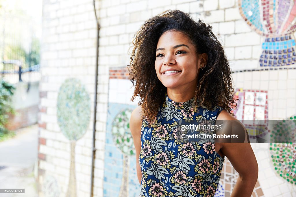 Smiling woman next to tiled mosaic wall.