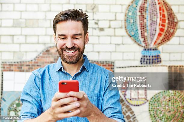 man with smartphone next to tiled mosaic wall. - happy man fotografías e imágenes de stock