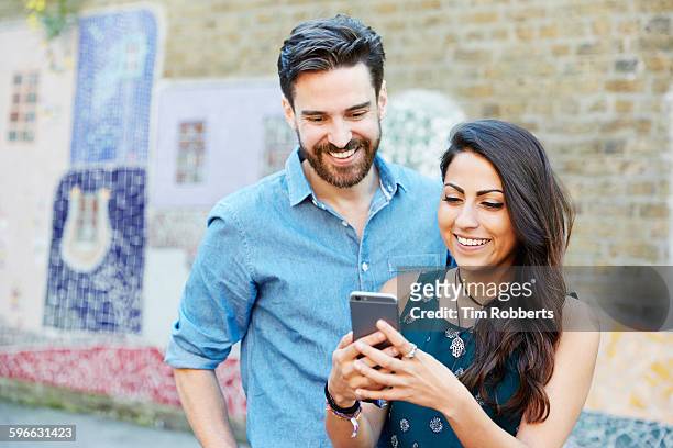 friends with smart phone next to mosaic wall. - indian woman phone stock pictures, royalty-free photos & images