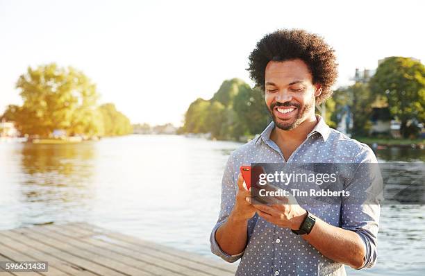 man using smartphone next to river. - london young people black and white stock-fotos und bilder