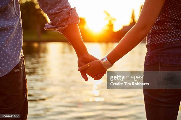 couple holding hands next to river. - darsi la mano foto e immagini stock