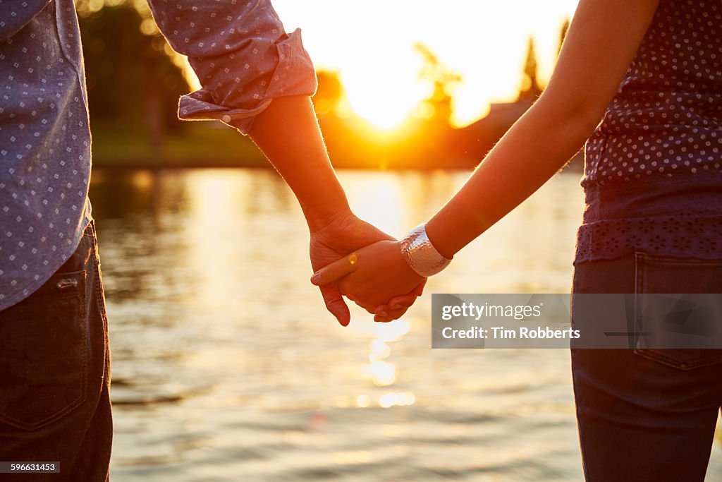 Couple holding hands next to river.