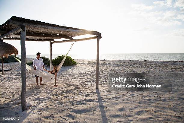 woman in hammock,man standing next to her. - beach hut stock pictures, royalty-free photos & images
