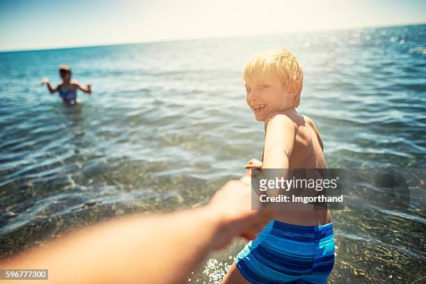kleiner junge zieht seinen vater ins meer - child and unusual angle stock-fotos und bilder