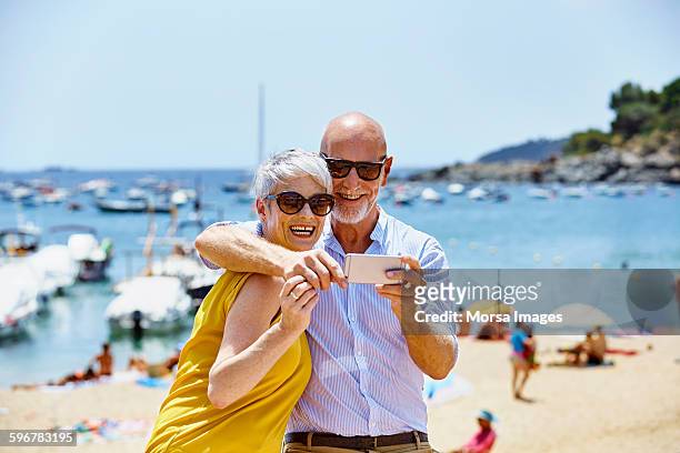 happy senior couple taking selfie on beach - happy couple using cellphone stockfoto's en -beelden