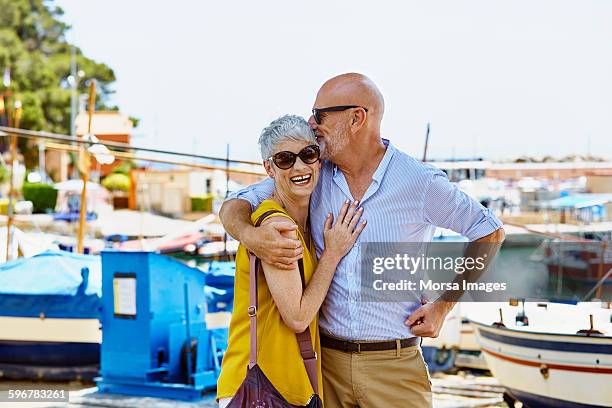 Loving senior man kissing woman against harbor