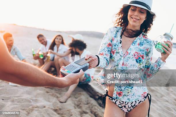 junge frau zahlt mit kreditkarte am strand - cocktail counter stock-fotos und bilder