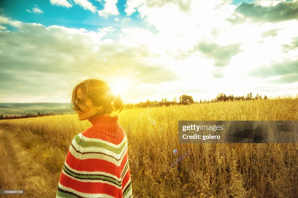 Woman with poncho in summer landscape at sunset hour