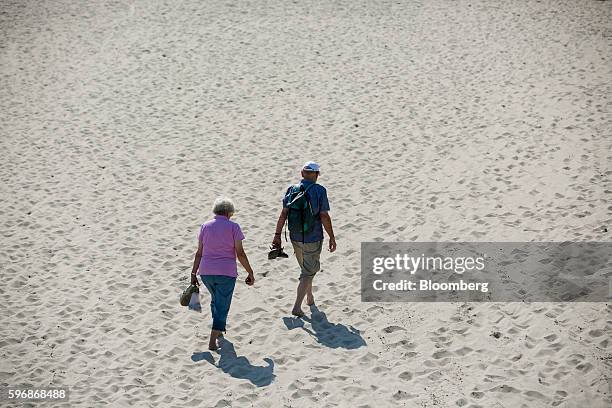 Pensioners carry their shoes as they walk barefoot along the sand on the beach in Sellin, Ruegen Island, Germany, on Saturday, Aug. 27, 2016....