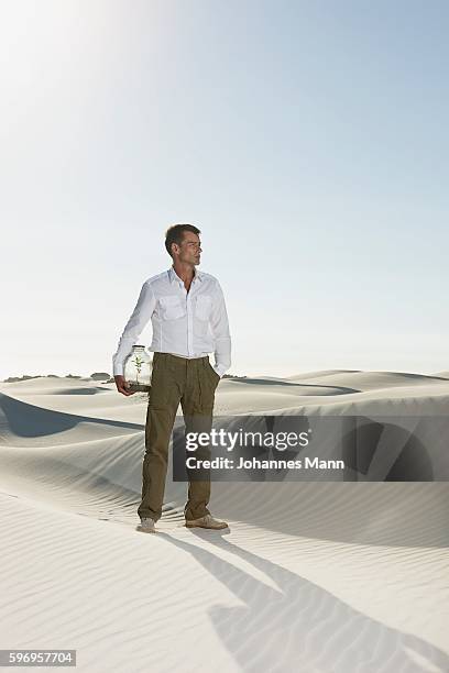 man carrying jar with plant in desert - pantaloni militari foto e immagini stock