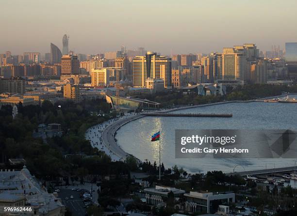 People walk along a promenage next to the Caspian Sea as the sun sets on the skyline in Baku, Azerbaijan, May 1, 2014.