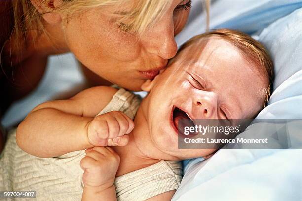 mother kissing laughing baby (9-12 months), close-up - baby light stock-fotos und bilder