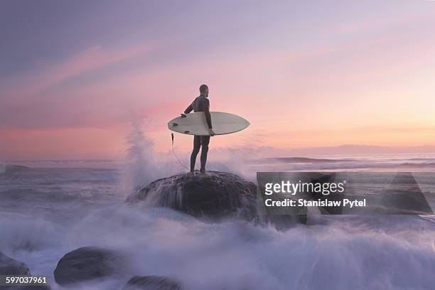 surfer on rock against sunset, water around - herausforderung stock-fotos und bilder