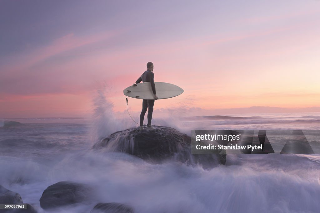 Surfer on rock against sunset, water around